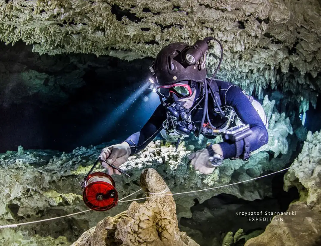 Technischer Höhlentaucher legt Führungsleine in einer Unterwasserhöhle mit Stalaktiten, CCR-Kreislaufgerät und Explorationslampe
