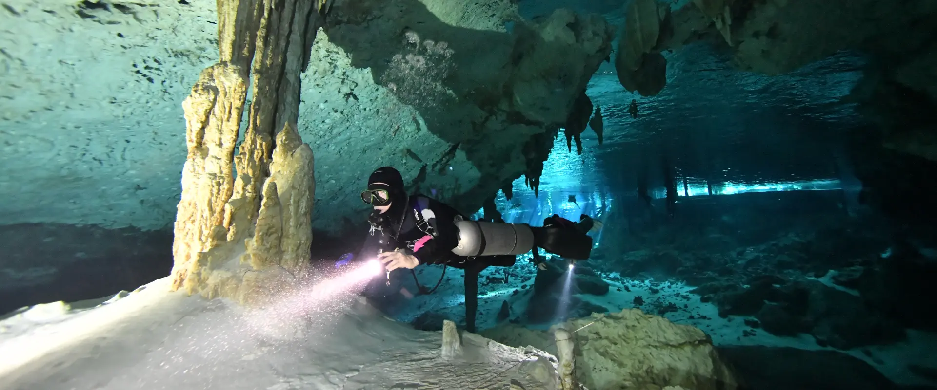 Buceador técnico en cueva subacuática iluminando formaciones de estalactitas y estalagmitas con luz primaria