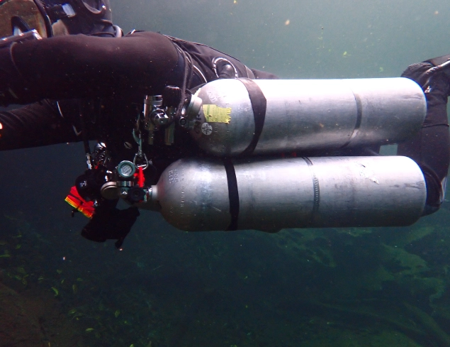 Buceador técnico de espeleobuceo instalando carrete guía en cueva subacuática con estalactitas, equipo de circuito cerrado CCR y luz de exploración<br />
